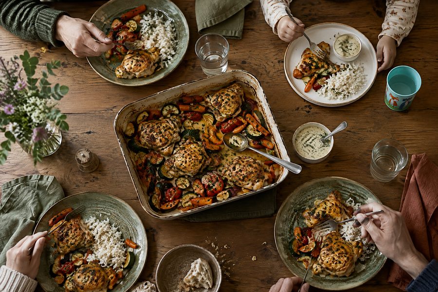 A family sharing one chicken, rice and roast vegetable dinner around a wooden table